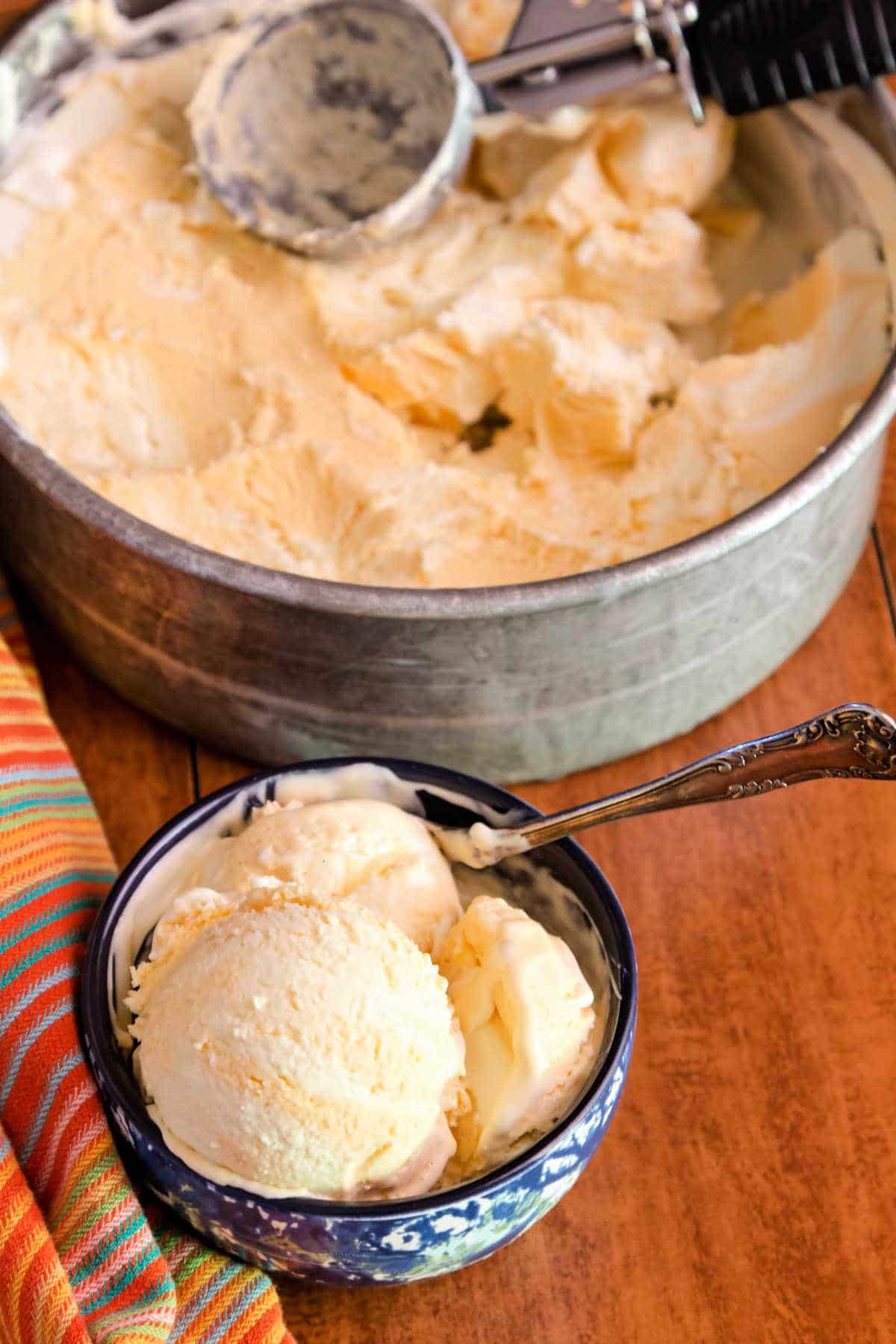 A dish of creamsicle ice cream with container and scoop in the background.