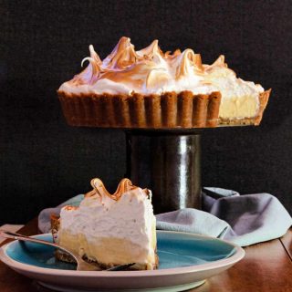 square image of lemon meringue pie on a pedestal and a slice on a plate