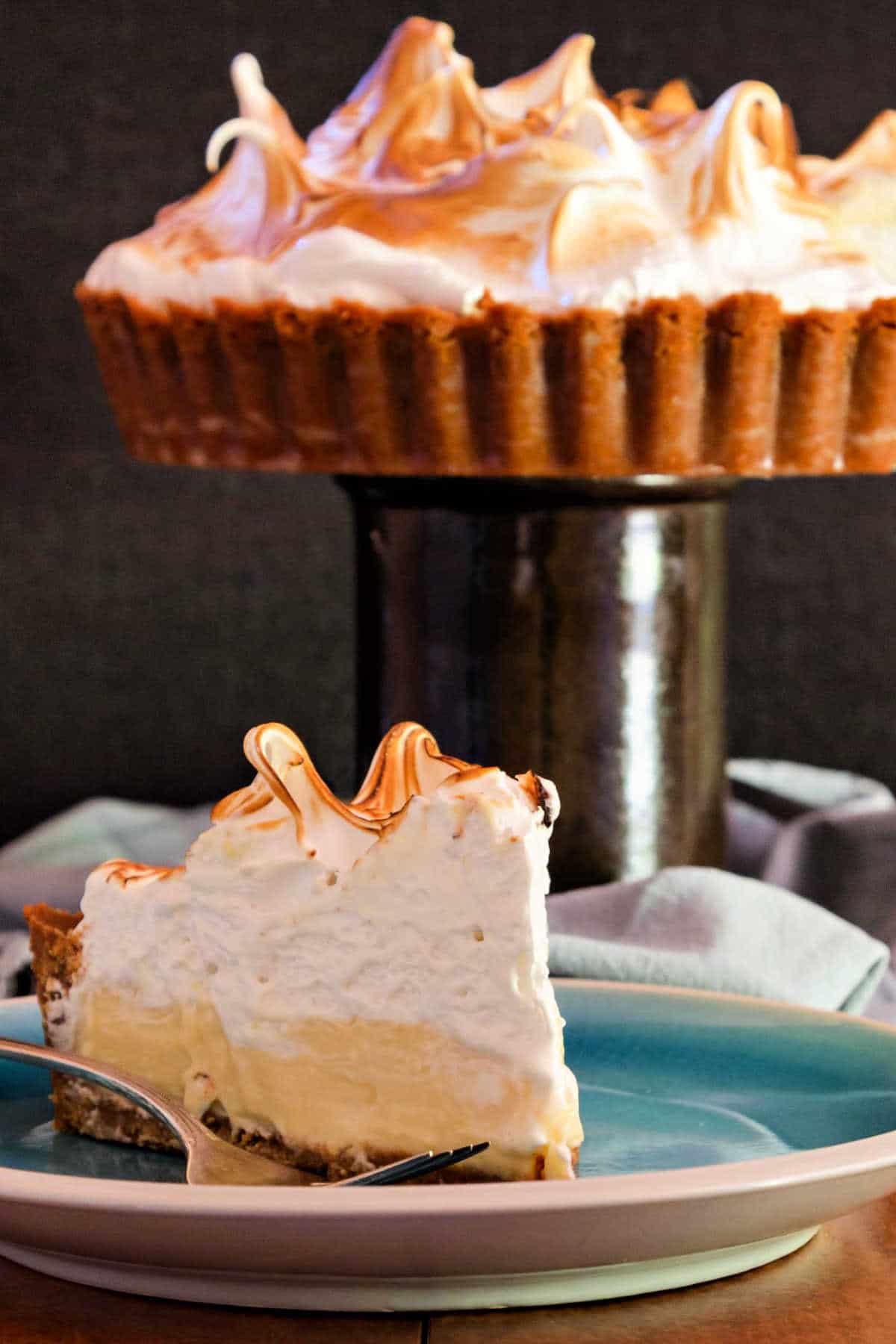 A slice of deep dish tart with a ton of meringue on a blue plate.