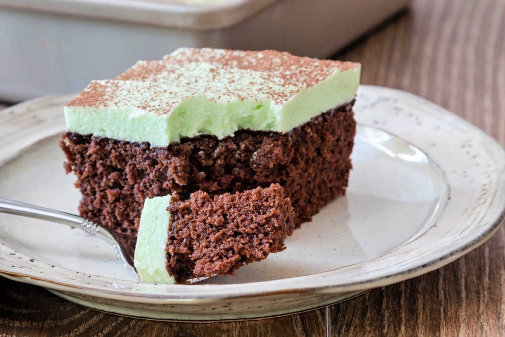 A square slice of cake with green frosting with a bite of cake on a fork.