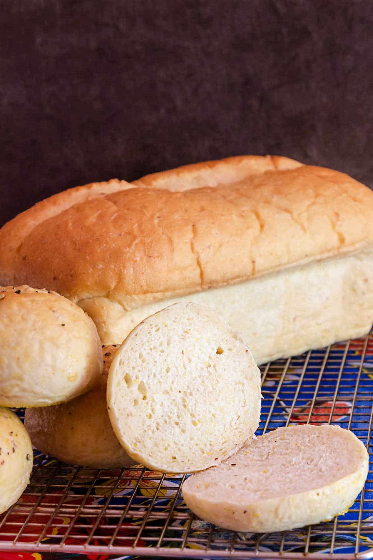 A fresh loaf of grits bread and a sliced bun on a cooling rack.