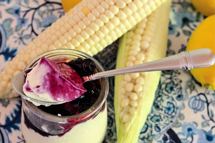 overhead shot of glass of lemon corn panna cotta with blueberry sauce with lemons and ears of corn in the photo