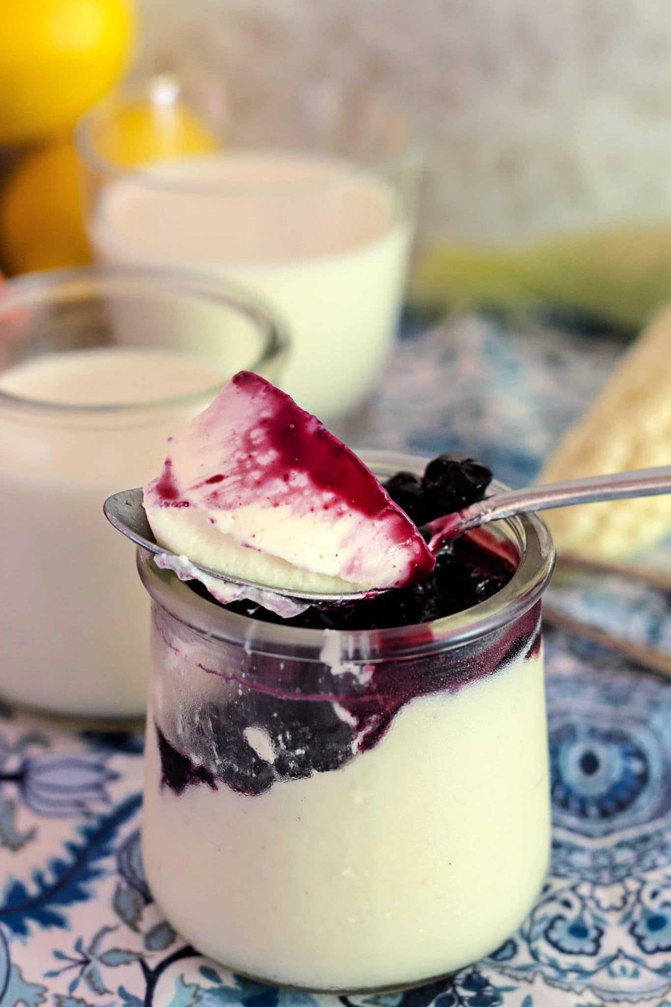 A single serving jar of lemon corn panna cotta with blueberry sauce and a bite on a spoon.