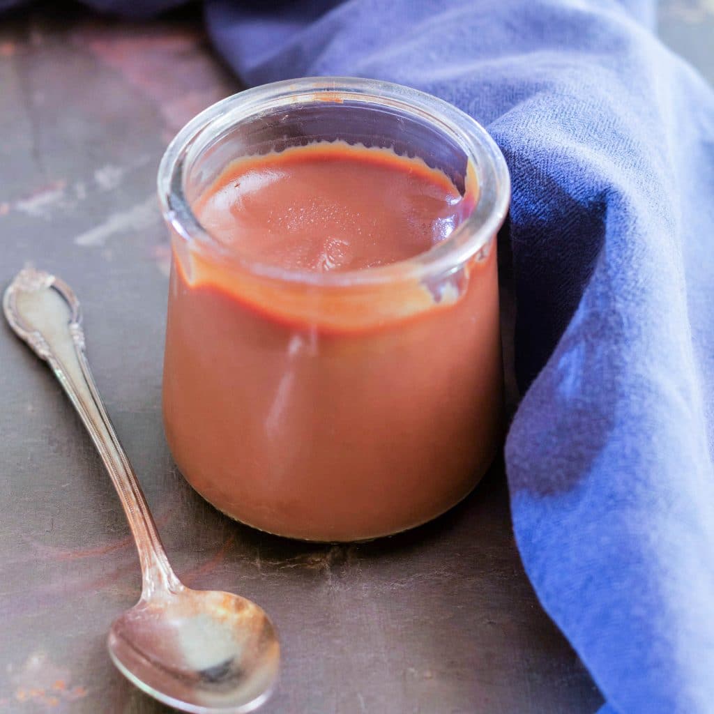 A glass jar of chocolate caramel pudding with spoon.