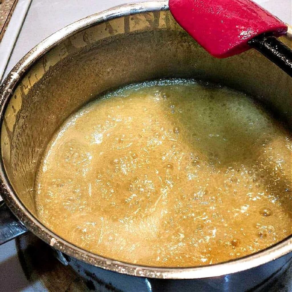 A pot of boiling cream, sugar, and butter that is a light caramel color.