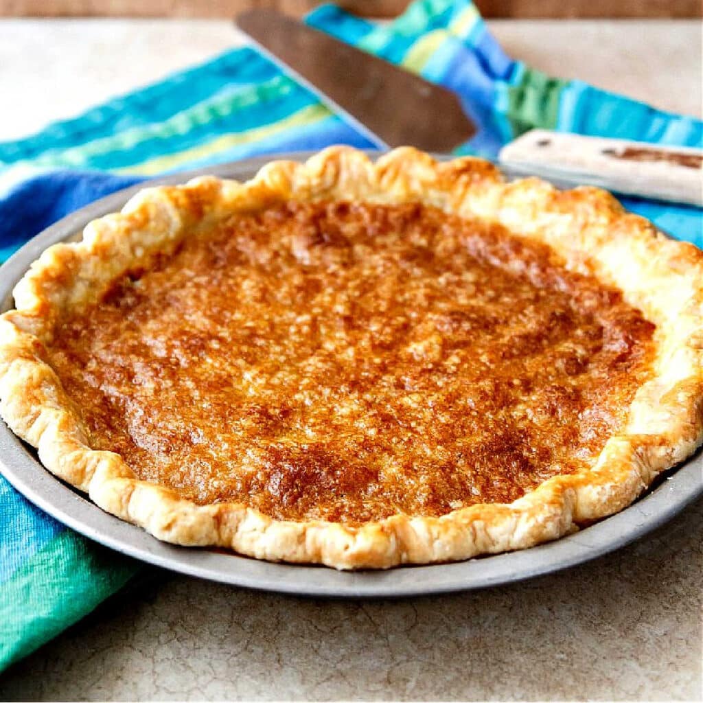 A whole pie in a fluted pie crust on a blue-striped napkin with a pie server.