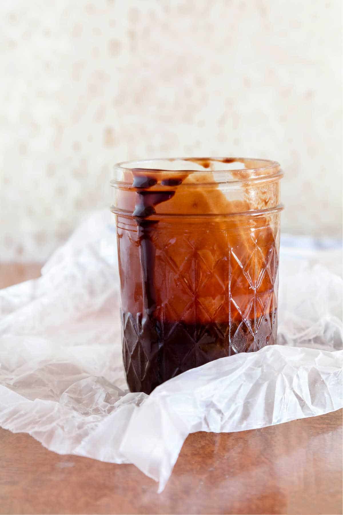 A mason jar half full of homemade chocolate syrup resting on a piece of waxed paper.
