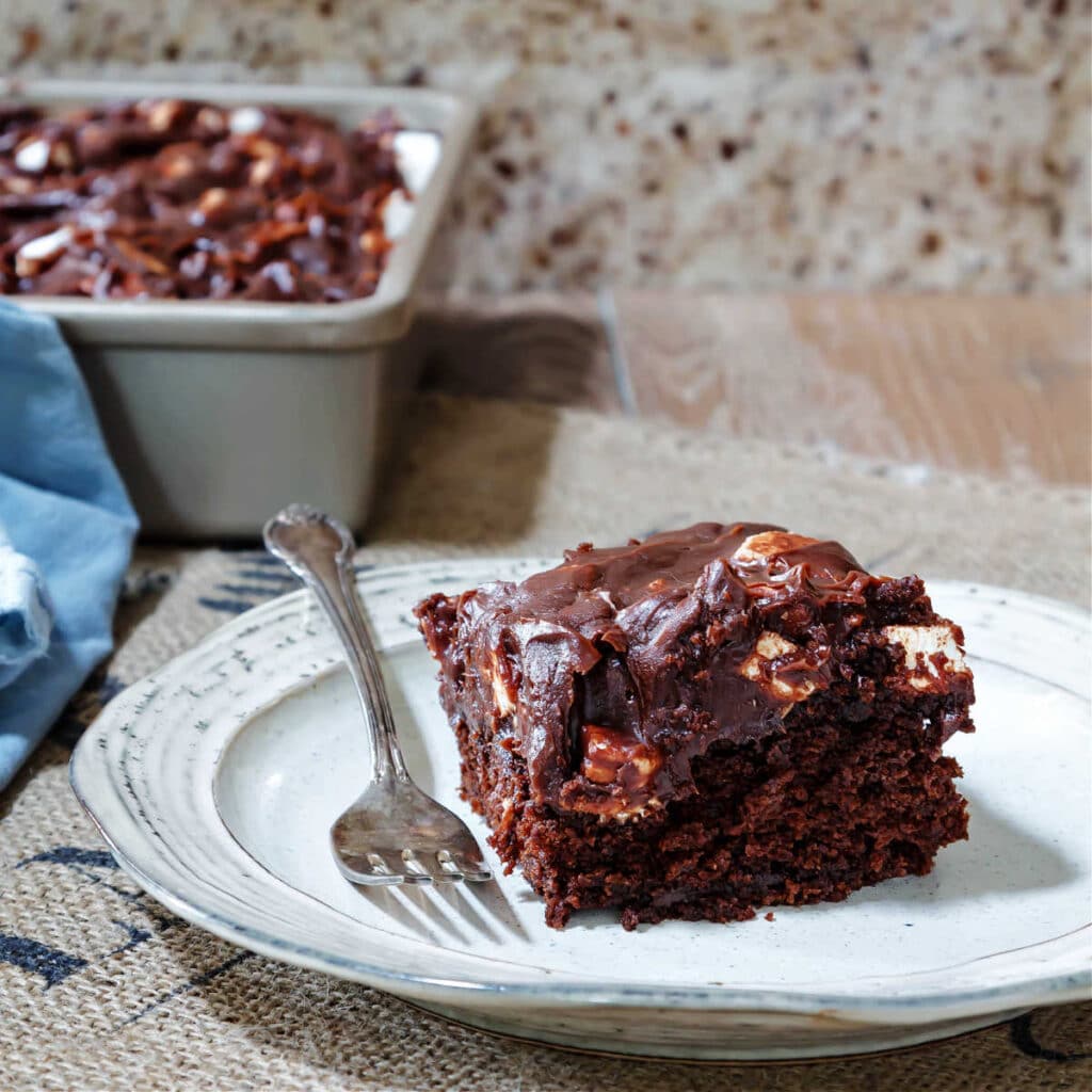 A piece of chocolate cake with chocolate frosting with mixed nuts and tiny marshmallows in it.