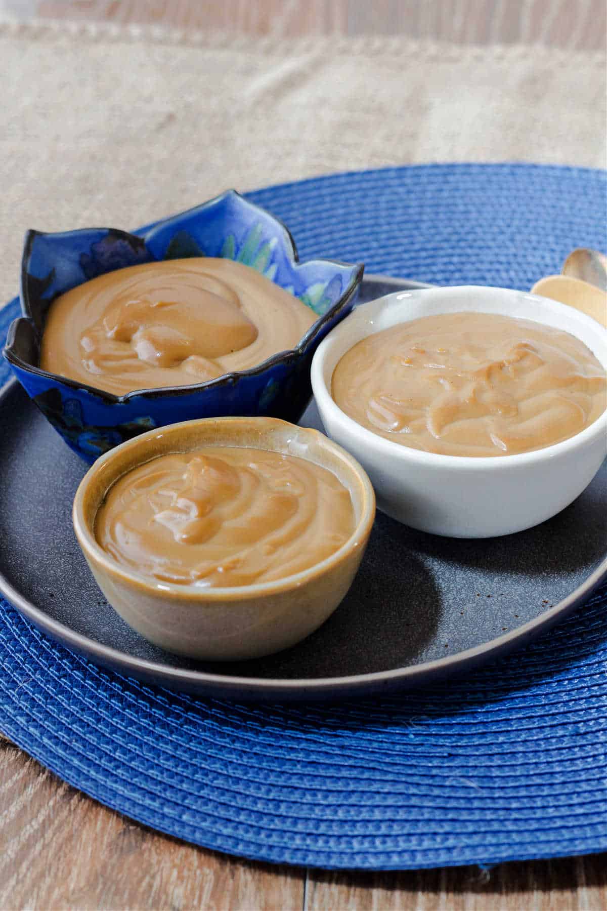 Three individual bowls of creamy butterscotch pudding on a serving plate, on a blue place mat.