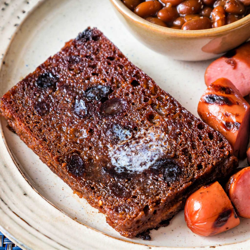 A slice of Boston brown bread, fried in butter with franks and a side of baked beans.