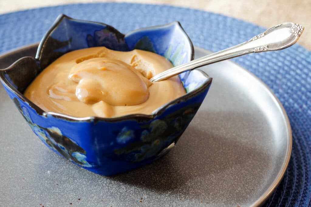 A single serving of butterscotch pudding in a blue scalloped pottery bowl with a silver spoon ready for eating.