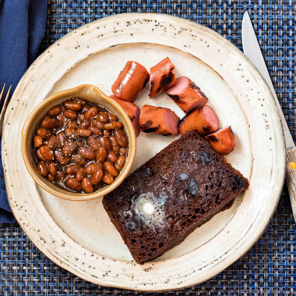 Overhead shot of Boston brown bread, grilled franks, and a bowl of baked beans ready for serving.