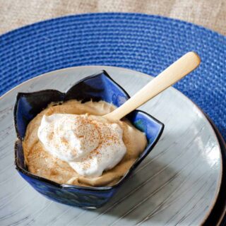 A bowl of butterscotch pudding in a blue bowl with a dollop of whipped cream and a sprinkle of cinnamon on top.