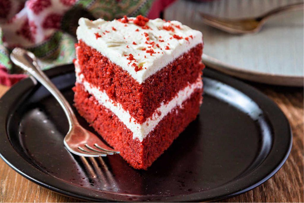 slice of red cake with white frosting on a black plate