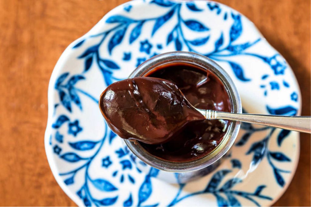 A  spoonful of chocolate pudding from a glass jar of pudding, against a blue patterned plate.