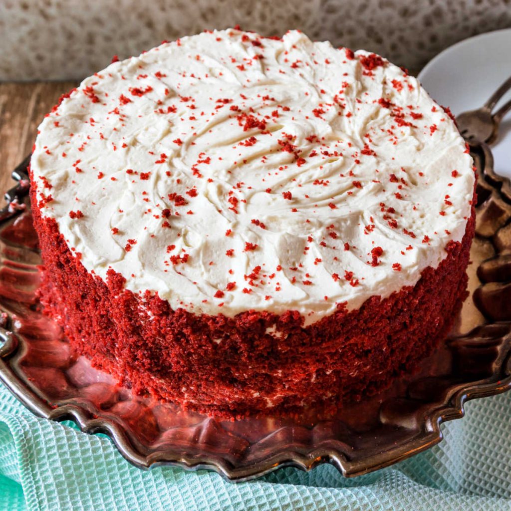 A whole cake frosted with ermine buttercream and decorated with red cake crumbs.