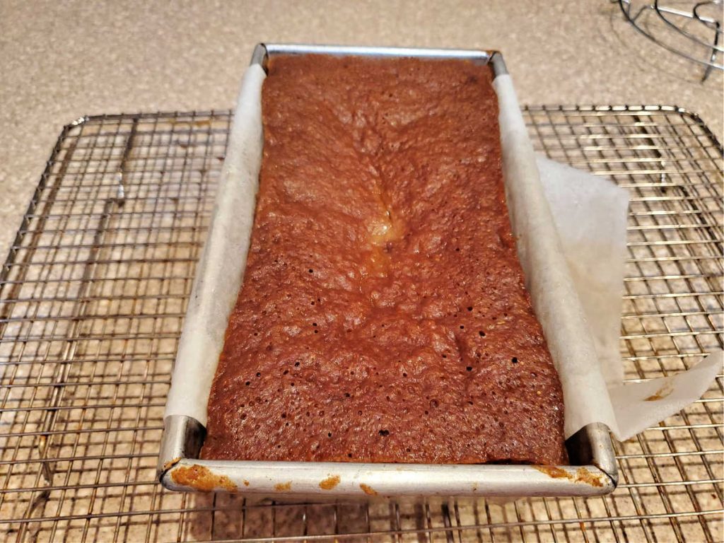 Steamed brown bread in a pan cooling on a rack.