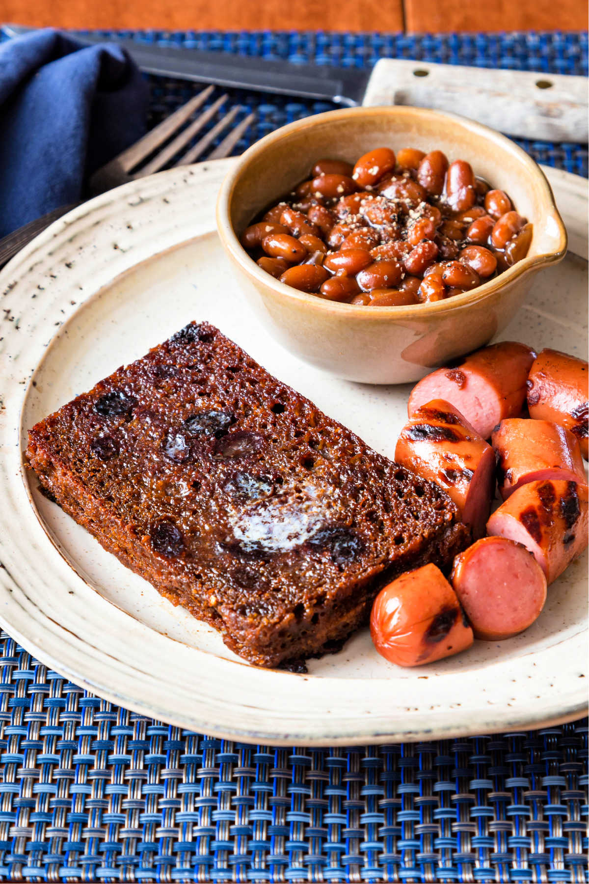 A slice of butter-fried Boston brown bread, grilled sliced franks, and a bowl of beans on a plate.