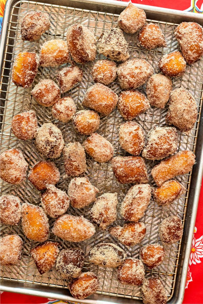A tray of donut holes tossed with pumpkin spice sugar coating, on a cooking rack.