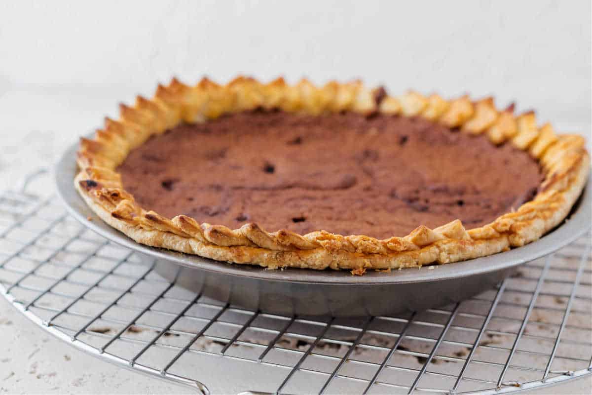 A whole chocolate chess pie in a metal pie pan cooling on a wire rack.