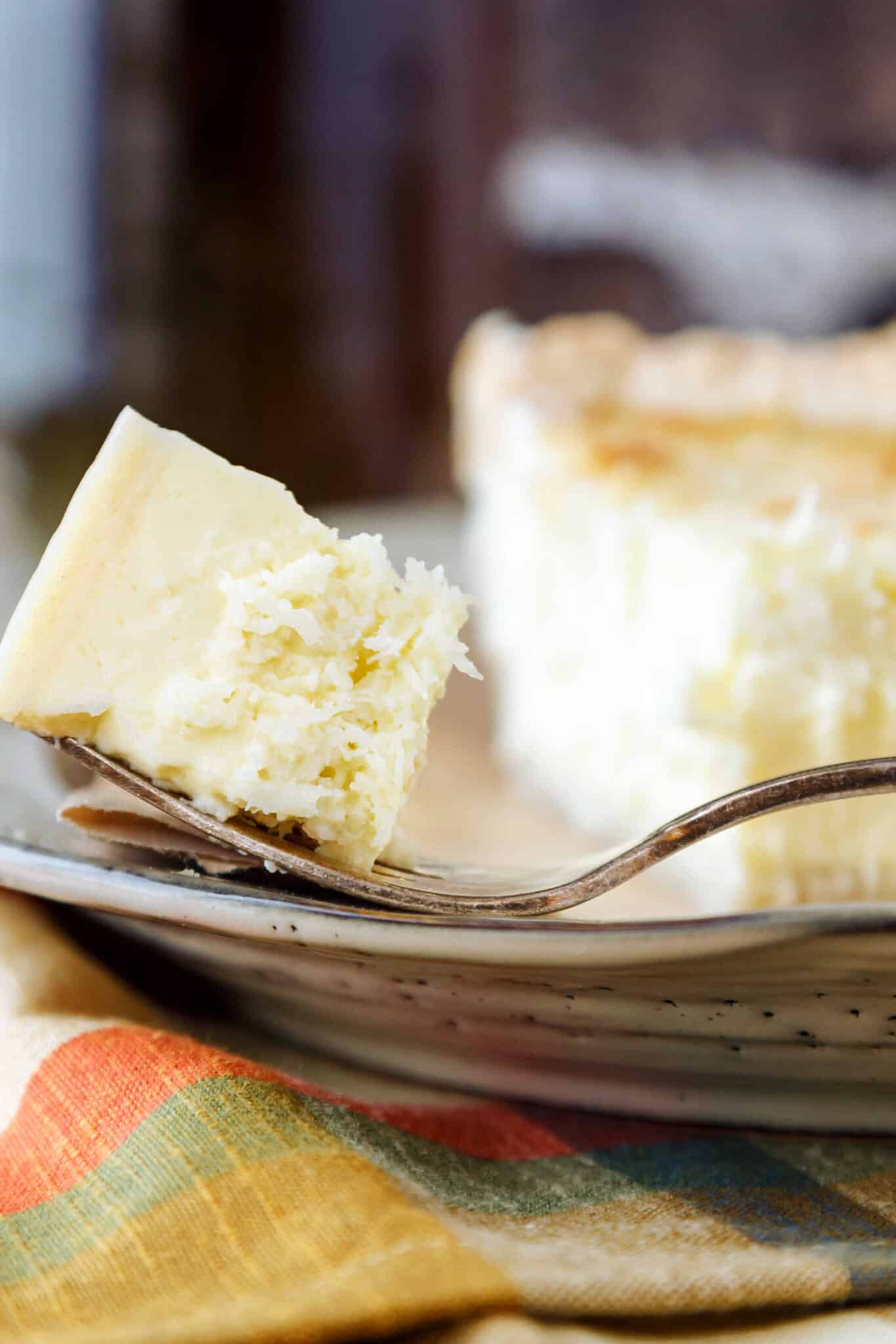 A bite of coconut custard pie on a fork on a plate with the rest of the piece of pie.