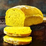 A square image of a sliced loaf of savory pumpkin bread showing the sunny interior and crumb structure.
