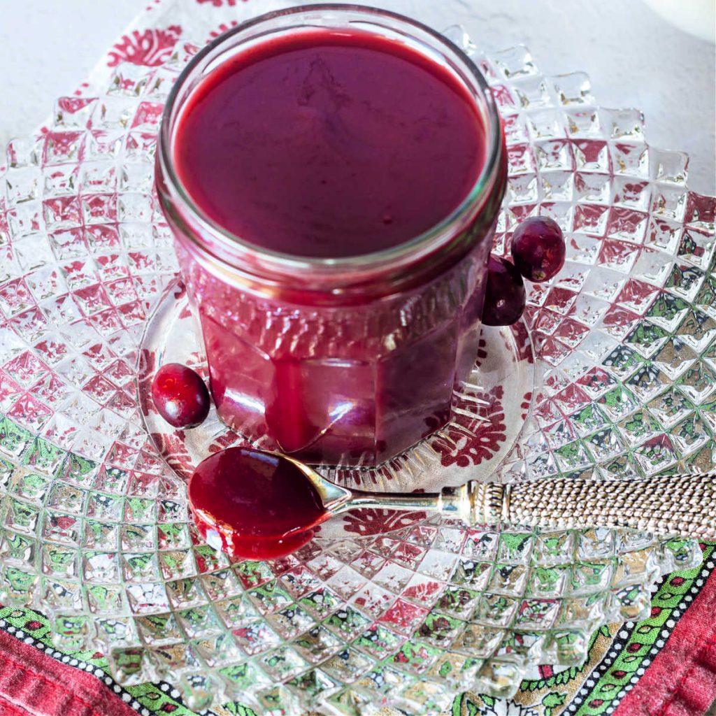 A spoonful of cranberry ketchup and a jar of same on a crystal plate.