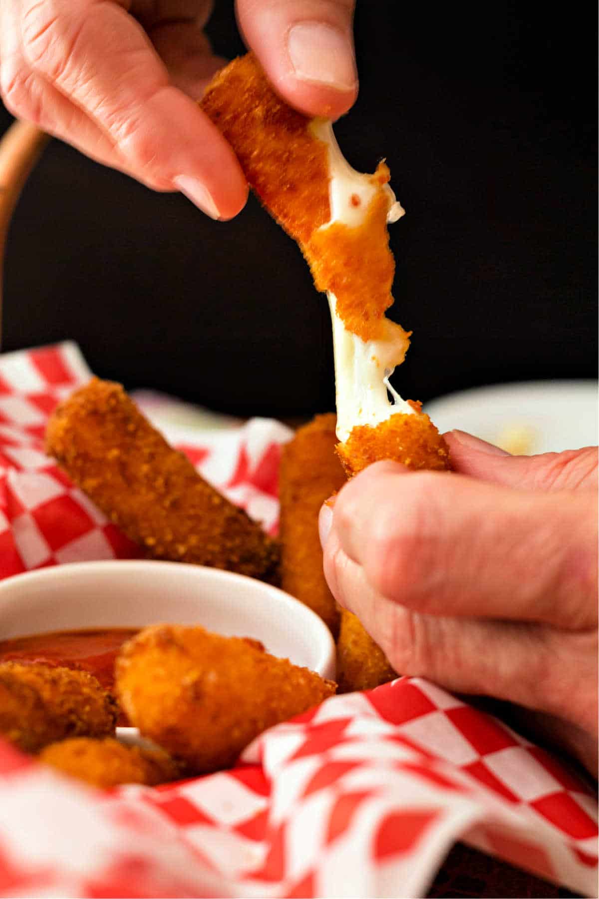 Close up of hands pulling a fried mozzarella stick apart to show the stretchy cheese insides.