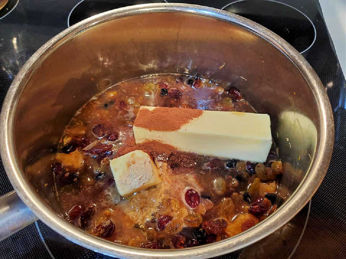 A pot with liquid, dried fruit, butter, and spices for making fruitcake.