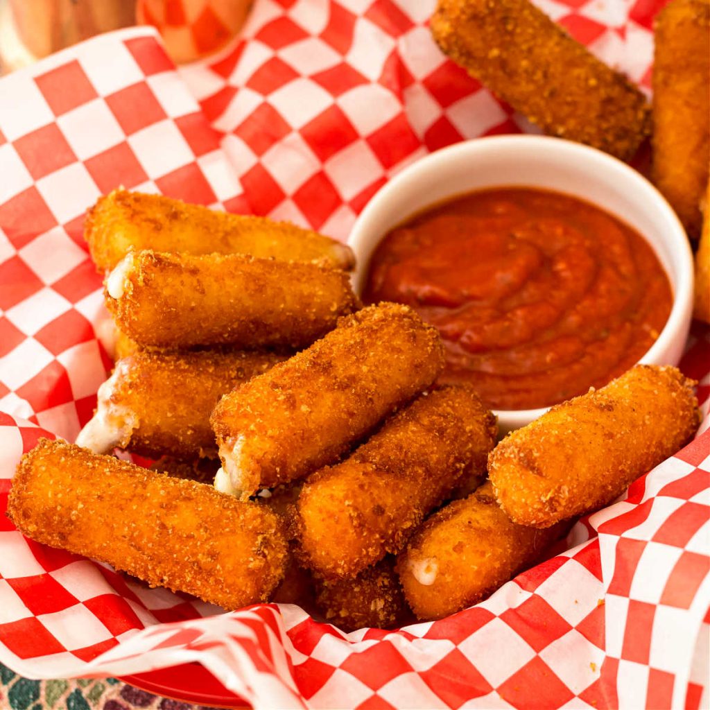 fried mozzarella sticks iwth marinara in a basket with a red and white checked paper liner