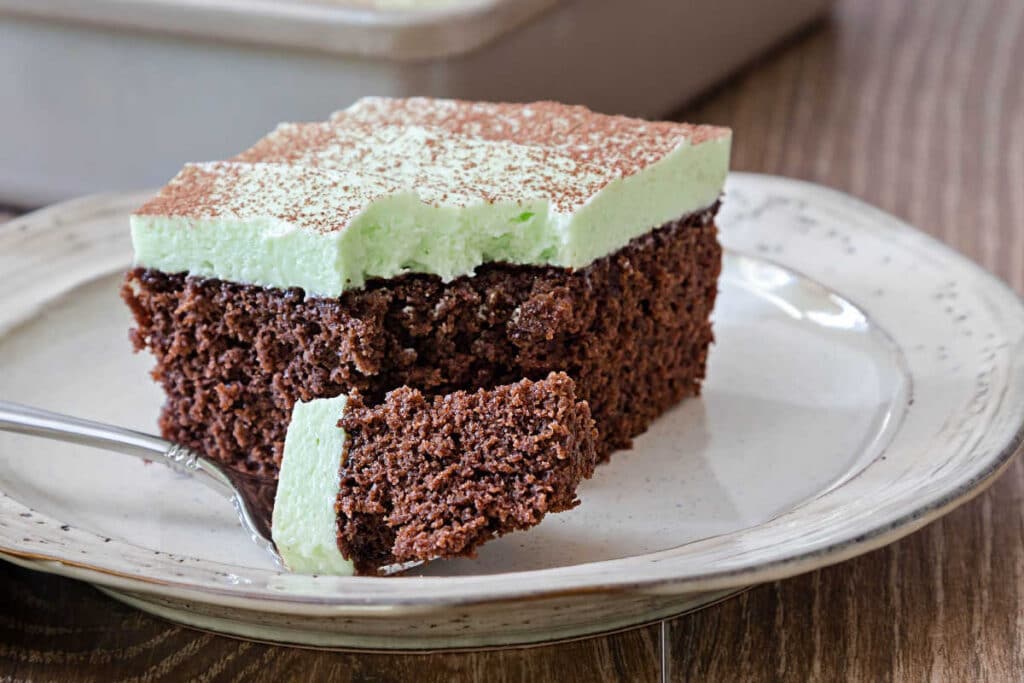A square of chocolate cake with pale green frosting on a plate.