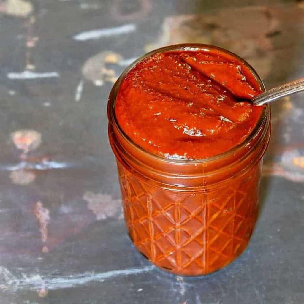 A jar of ketchup with a spoon in it.