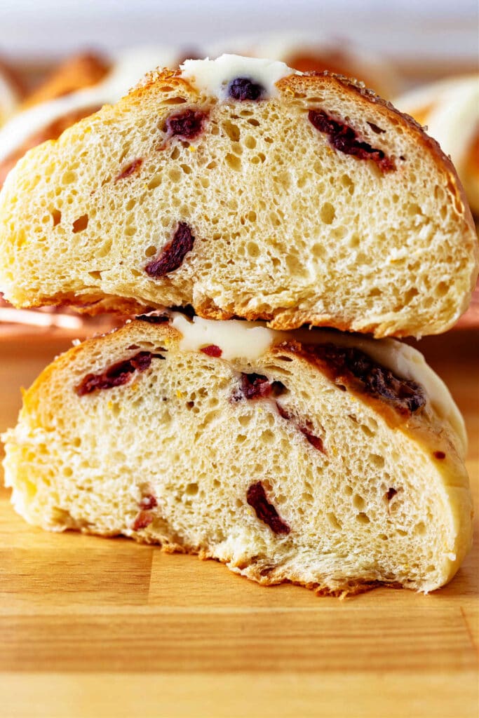 A hot cross bun cut in half to show the interior crumb and the dried cranberries throughout.