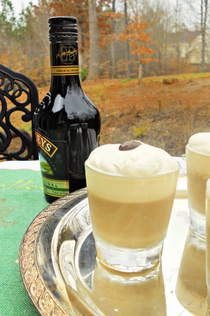 A silver tray with individual Irish cream panna cottas topped with chocolate c covered espresso beans. Tray is on a table outside in fall weather. A bottle of Irish cream is next to the tray.
