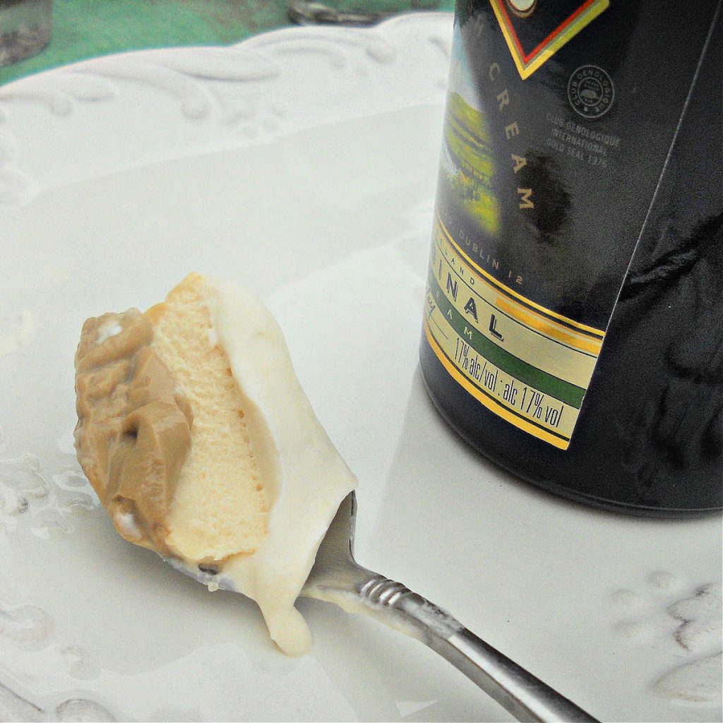 A bite of Irish Cream panna cotta on a spoon showing the three layers of the dessert. A bottle of irish cream is next to the spoon.