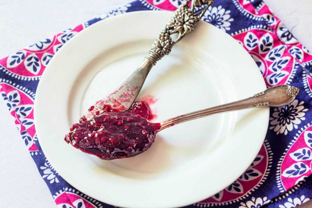 A spoonful of jam on a spoon with a spreader on a white plate.