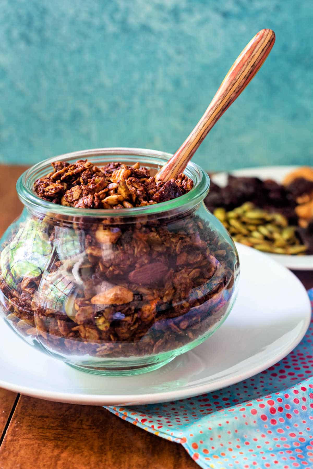 A jar of chocolate granola iwth a wooden spoon in it.