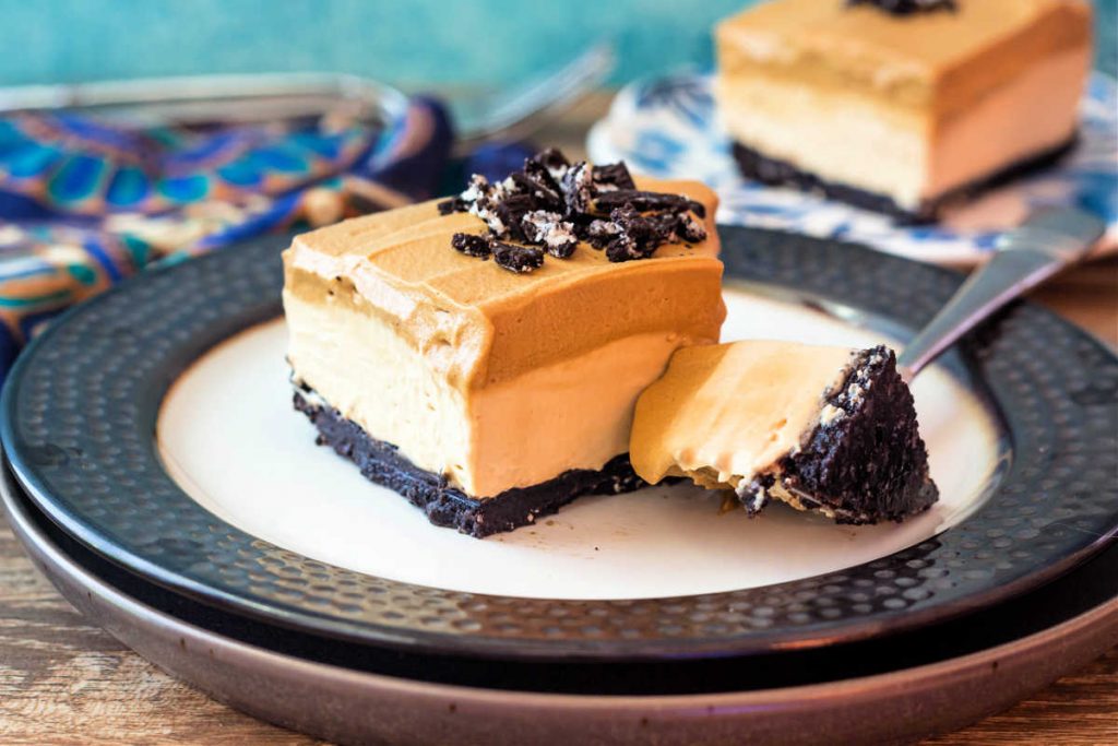 A square whipped coffee cheesecake bar on a plate with a bite of the dessert on a fork.