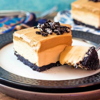 A square whipped coffee cheesecake bar on a plate with a bite of the dessert on a fork.