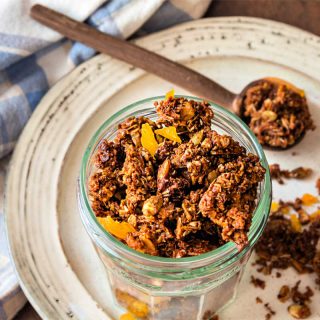 A jar of granola with pieces of apricot on a beige plate.