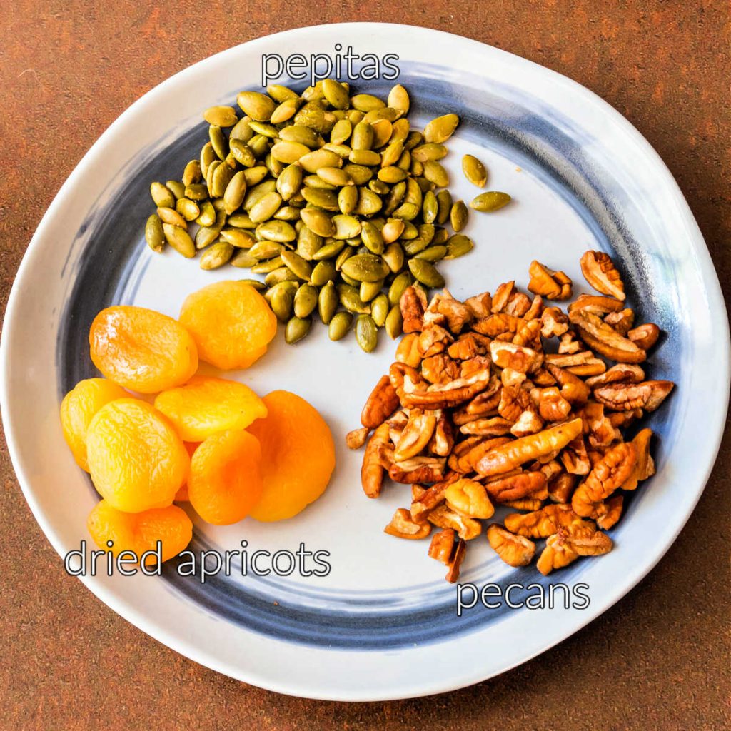 An overhead shot of a blue plate with pepitas, pecans, and dried apricots on it.