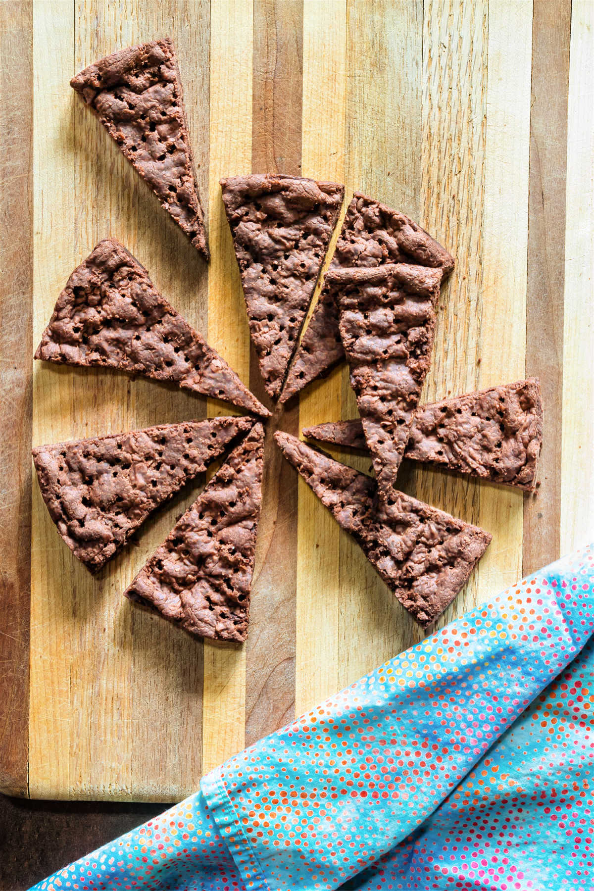 An overhead shot of triangles of chocolate chip shortbread on a cutting board with a blue napkin.