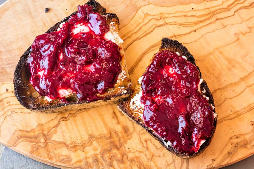 An overhead shot of two halves of a slice of artisan bread, toasted, spread with goat cheese and plum chutney.