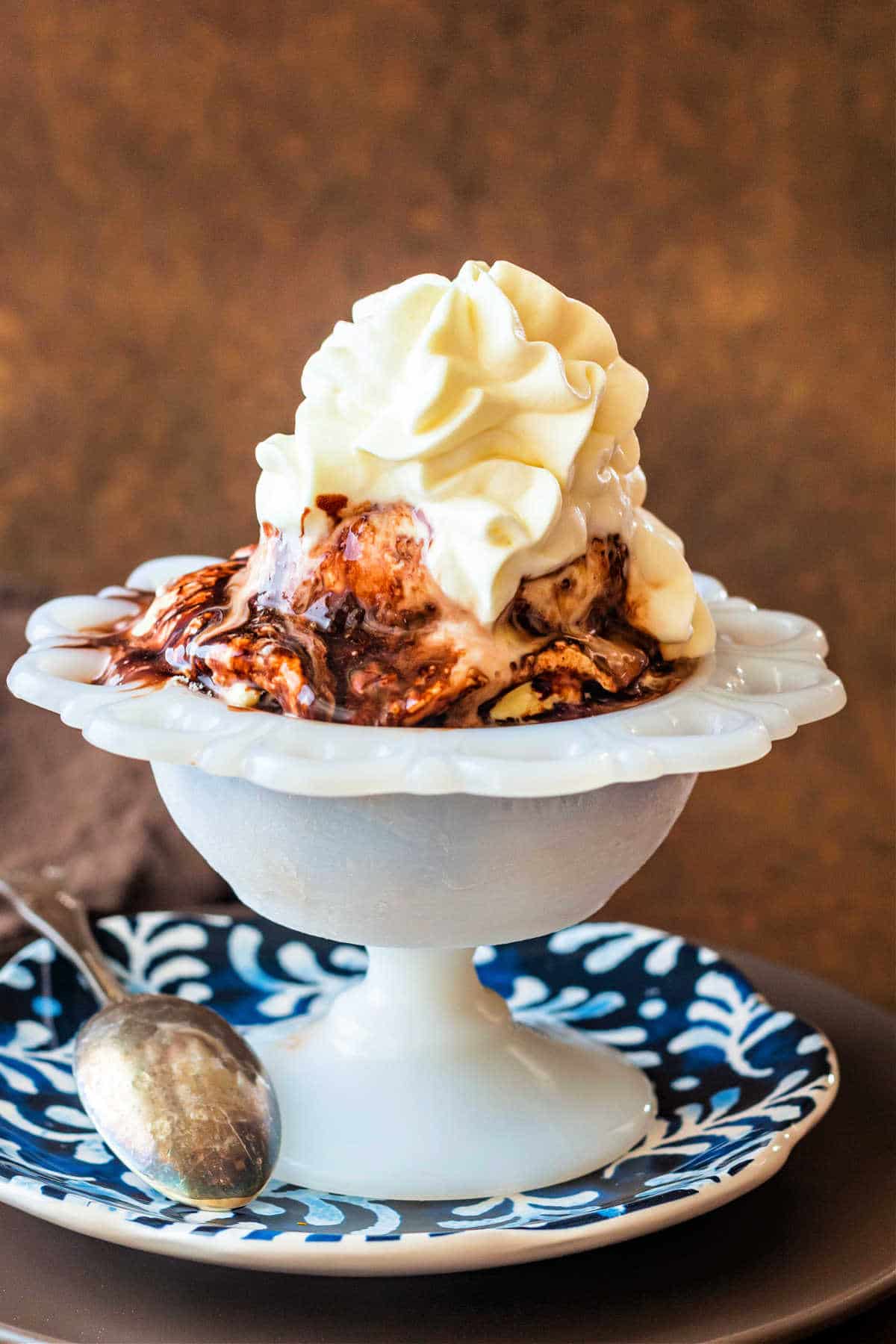 A shot of ice cream in a white dish with chocolate syrup and whipped cream on top.