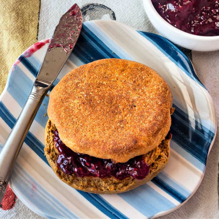 An overhead shot of a split English muffin with jam on it on a striped blue plate.