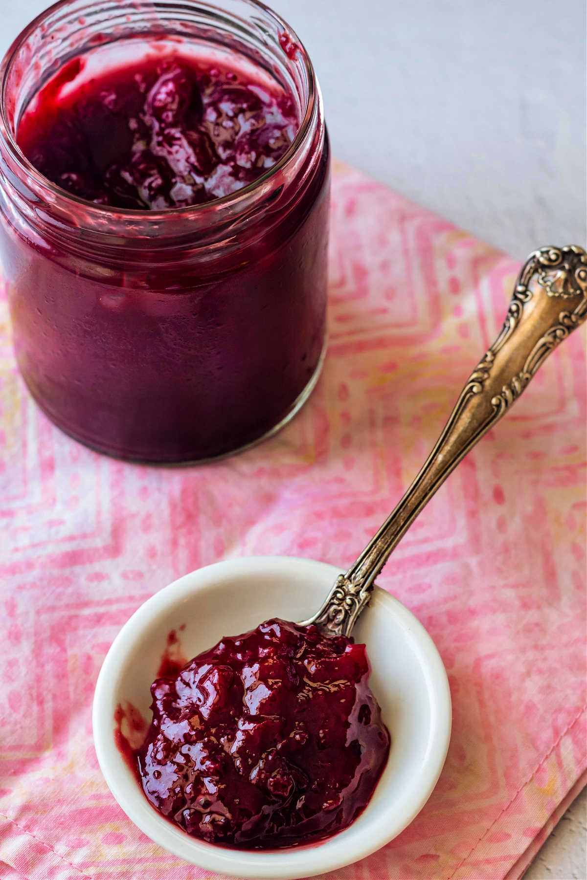 A jar of plum jam with a spoonful of the jam in a small white dish.