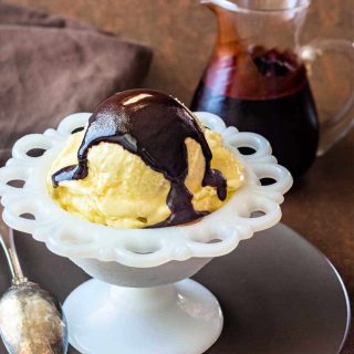 A scoop of custard-based vanilla ice cream in a white, lacy bowl with chocolate syrup on top.