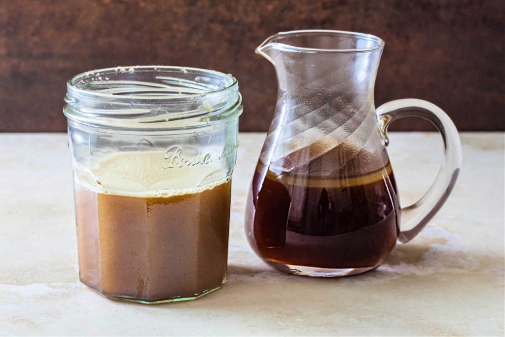 A jar of butterscotch syrup next to a small pitcher of syrup. The syrup in the jar is more opaque than the syrup in the pitcher, which has a smll amount of melted butter floating on the top.
