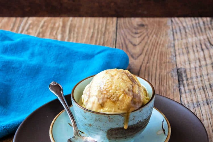 A blue bowl of butterscotch ripple ice cream on a wooden background.