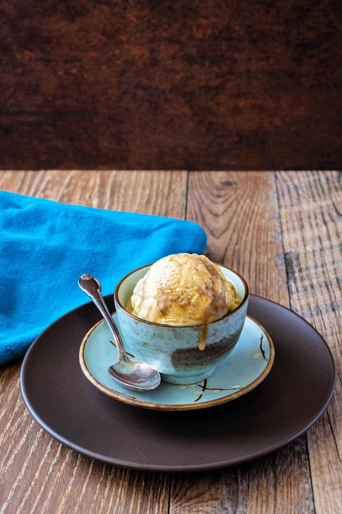 A blue bowl of butterscotch ripple ice cream on a wooden background.